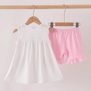 A girl's two-piece outfit hanging on wooden hangers from a light wood rod. The set includes a sleeveless white dress with tiny polka dots and matching light pink ruffle-trimmed shorts.