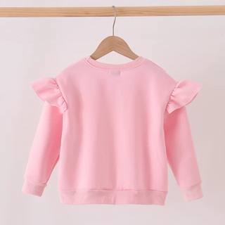 A light pink long-sleeve sweatshirt with ruffled shoulder details, hanging on a wooden hanger from a wooden clothes rack against a plain white background.