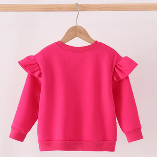 A bright pink long-sleeve sweatshirt with ruffled shoulder details, hanging on a wooden hanger from a light wood rod against a plain white background.
