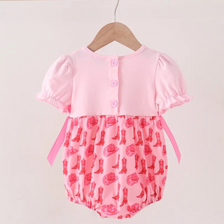 A baby romper hanging on a wooden hanger against a plain light background. The romper has a solid light pink upper section with three front buttons and short ruffled sleeves, paired with a pink patterned lower section featuring cowboy boots and roses.