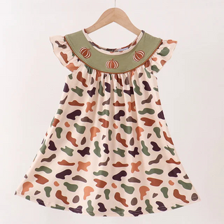 A toddler girl's dress with a multicolor abstract print on a cream background, featuring a solid sage green collar with embroidered orange details, hanging on a wooden hanger against a white wall.
