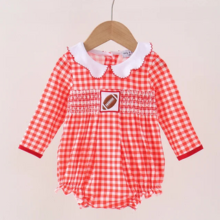 A baby girl's long-sleeve romper in a red and white gingham pattern, featuring a white ruffled Peter Pan collar and a smocked chest detail with a football patch, hanging on a wooden hanger.