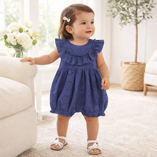 Baby girl wearing a blue eyelet romper in a bright living room