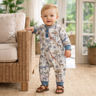 Child wearing a jungle-themed onesie standing in a room with wicker furniture and plants.
