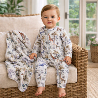 Child wearing a jungle safari patterned onesie sitting on a couch with a blanket