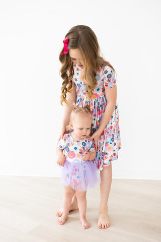 Two young girls in matching floral dresses standing on a white background