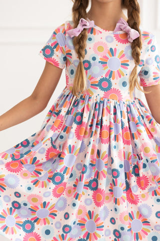 Child wearing a colorful floral dress with ruffled sleeves against a white background