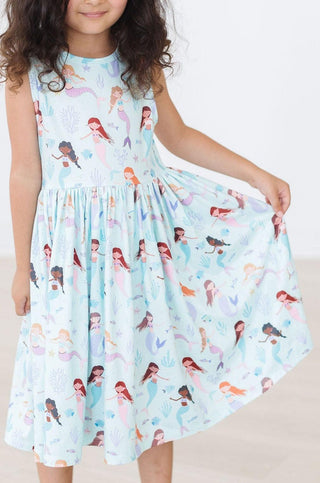 Child wearing a dress with mermaid pattern on a plain background