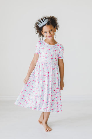 Young girl wearing a mermaid print dress on a plain background