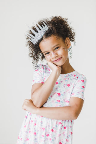 Young girl wearing a mermaid print dress and tiara with a white background