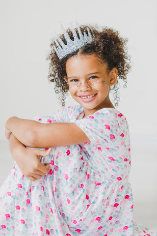Child wearing a mermaid print dress and tiara with a plain background