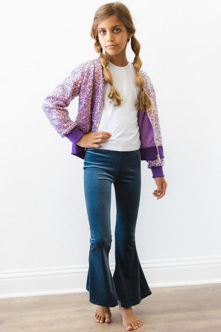 Young girl wearing a sequin jacket, white shirt, and blue jeans on a plain background