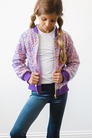 Girl wearing a colorful sequin jacket over a white shirt and blue jeans on a white background