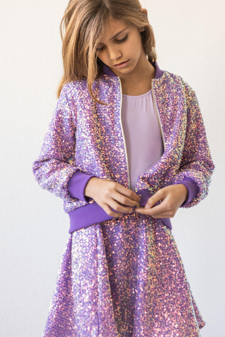 Young girl wearing a sparkly purple jacket against a white background