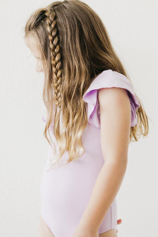 Young girl wearing a light purple leotard with ruffled sleeves against a white background