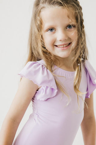 Young girl wearing a light purple leotard with ruffled sleeves against a white background