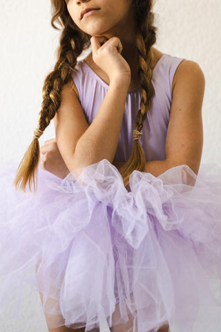 Young girl in a lavender leotard with a tutu sitting on a white background