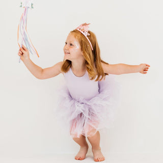 Young girl in a purple tutu leotard holding a wand against a white background