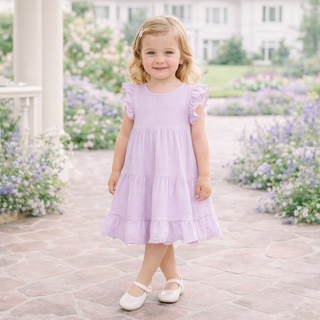 Young girl in a lavender dress standing in a garden with flowers.