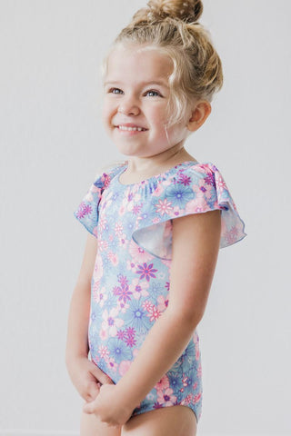 Young girl wearing a floral leotard with ruffled sleeves on a light background