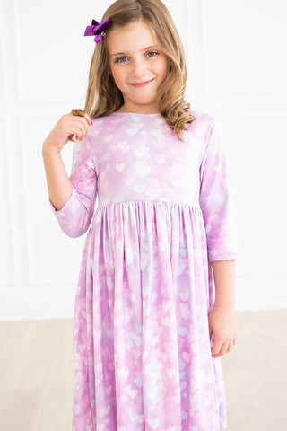 Young girl wearing a pink and purple patterned dress with a white background