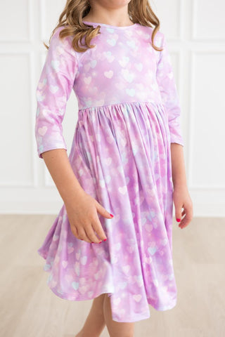 Child wearing a pink dress with heart patterns on a white background
