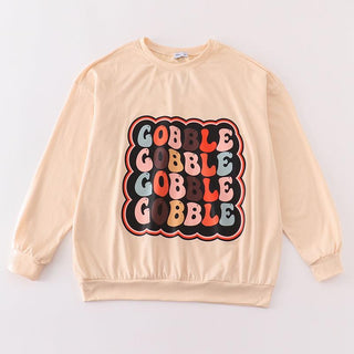 A beige women's long-sleeve top with a playful gobble print in various colors positioned centrally on the chest area.