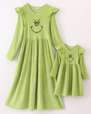 A green velvet Christmas-themed dress with embroidered character smiling at the top, presented in two different sizes, with the smaller size shown beside the larger one.