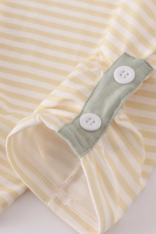 Close-up of a yellow and white striped garment with a green band and buttons on a light background