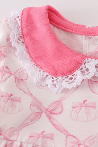 Close-up of a pink collar with lace trim on a fabric background with bow patterns.