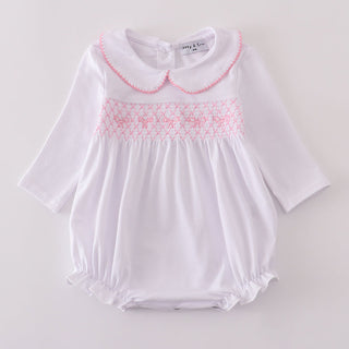 White baby romper with pink smocking on a light gray background