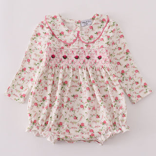 Floral baby romper with smocked details on a light gray background