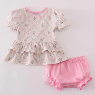 Baby outfit with a ruffled top and pink bloomers on a light gray background