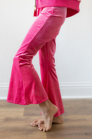 Person wearing bright pink pants on a wooden floor with a white wall background