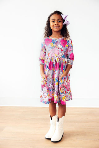 Young girl wearing a colorful floral dress with white boots on a plain background