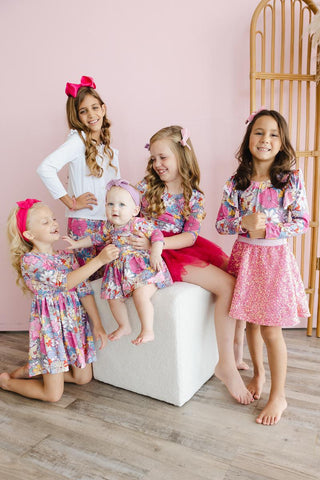 Five young girls in matching outfits posing together in a room with pink walls.