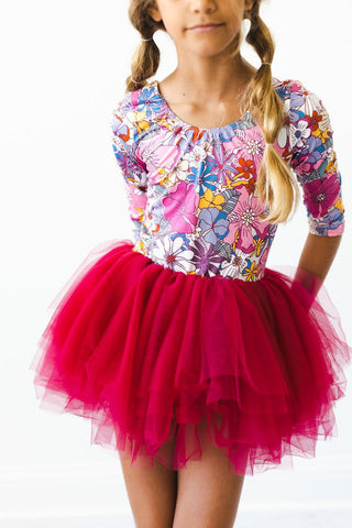 Young girl wearing a colorful floral leotard and mauve tutu skirt on a white background