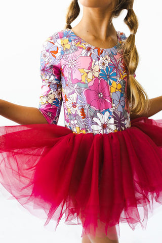 Child wearing a colorful floral leotard and mauve tutu skirt on a white background