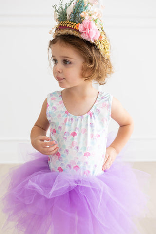 Young girl in a leotard and purple tutu with a decorative headband on a white background