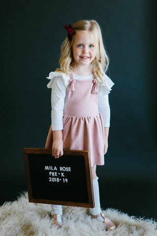 Young girl in a pink dress holding a blackboard with text on a dark background