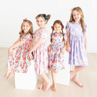 Four young girls wearing floral dresses standing on a white background