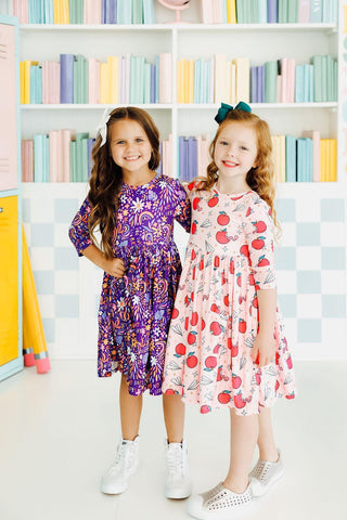 Two young girls in colorful dresses standing in front of a bookshelf with books.