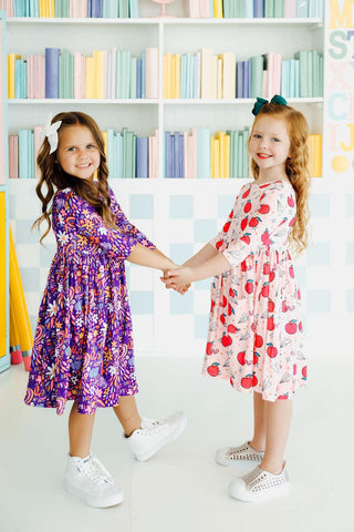 Two young girls holding hands in front of a bookshelf with colorful books.