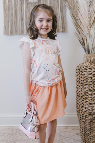 Young girl in a colorful outfit standing indoors next to a woven basket.