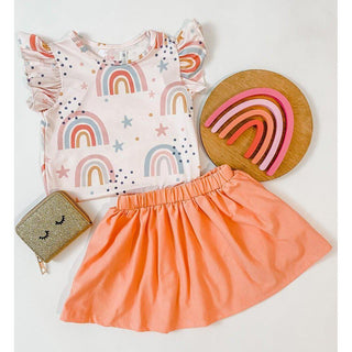 Children's outfit with rainbow-patterned top and orange skirt, accompanied by a wooden plate with rainbow design and small pouch.