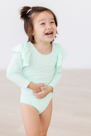 Child wearing a light green leotard with ruffled sleeves on a plain background