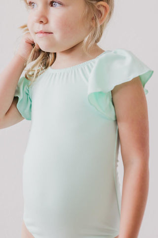 Young girl wearing a light green leotard with ruffled sleeves against a plain background