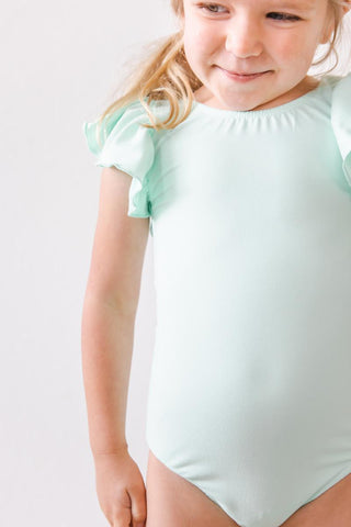 Young girl wearing a light green leotard against a plain background