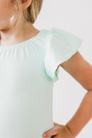 Child wearing a light green leotard with ruffled sleeves on a white background