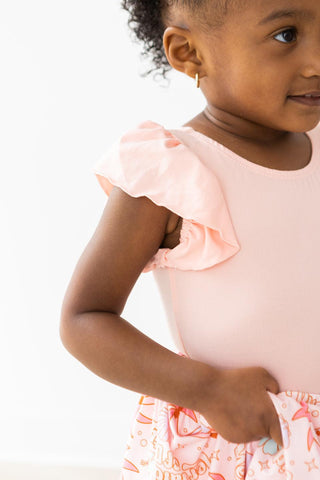 Young girl wearing a pink leotard with ruffled sleeves on a white background